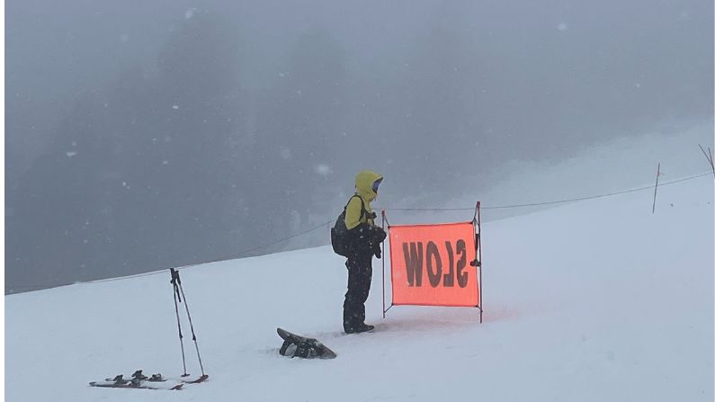 A ski resort employee stands by a "slow" sign.