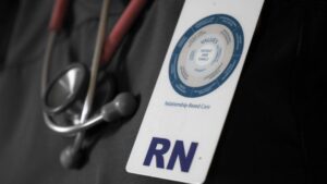 A registered nurse's badge and stethoscope. The badge details a relationship-based care model.